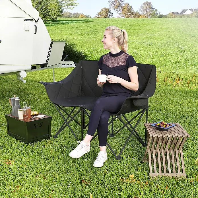 Outsunny Campingstuhl - 600D Oxford-Gewebe, Metall, Klappbar, Schwarz - Schwarzer Doppel-Campingstuhl aus Stoff in Nutzung im Freien, eine Frau sitzt bequem am Wohnwagen.