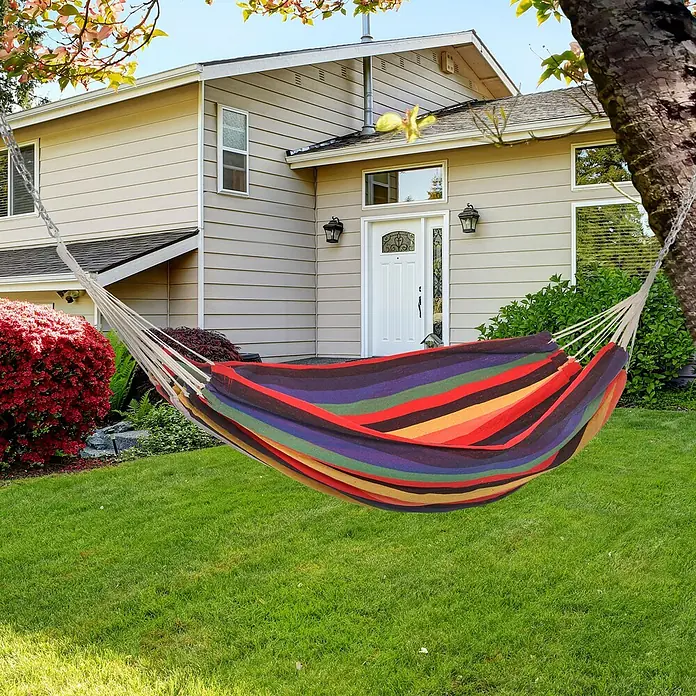 Outsunny Hängematte - L x B: 290 x 150 cm, Textil, Mehrfarbig, Passend für: für draußen - Eine bunte gestreifte Stoff-Hängematte hängt in einem grünen Garten zwischen einem Baum und einer Kette vor einem Haus.