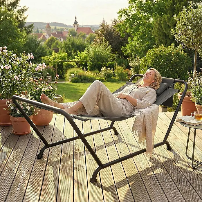Furnicato Hängesessel - L x B x H: 237 x 237 x 92 cm, Dunkelgrau - Frau entspannt sich in einem dunkelgrauen Hängesessel mit schwarzem Metallgestell auf einer Holzterrasse.