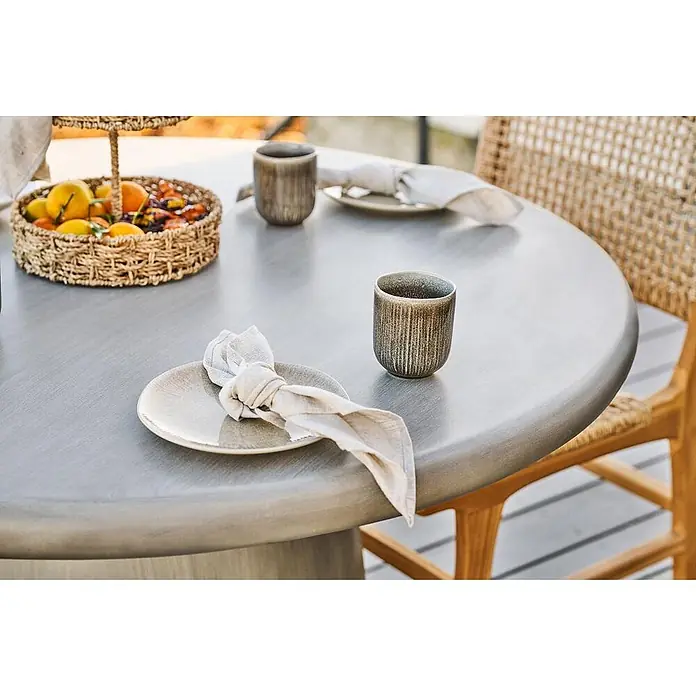 Ebuy24 Gartentisch rund Bente - Ø x H: 120 x 75 cm, 95% MgO, 5% Glasfaser, Grau, Stapelbar - Runder grauer Esstisch mit Holztextur, gedeckt mit Geschirr und Obstkorb.