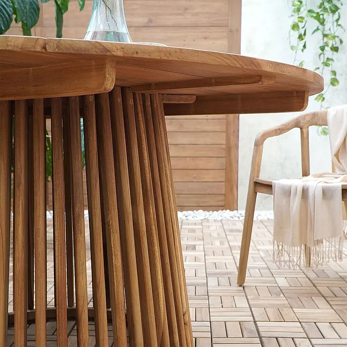 Ebuy24 Gartentisch rund Lorca - Ø x H: 120 x 75 cm, Teak, Natur, Stapelbar - Nahaufnahme eines runden Outdoor-Tisches aus Naturholz mit Lattenfuß, auf einer Terrasse mit Holzfliesen.