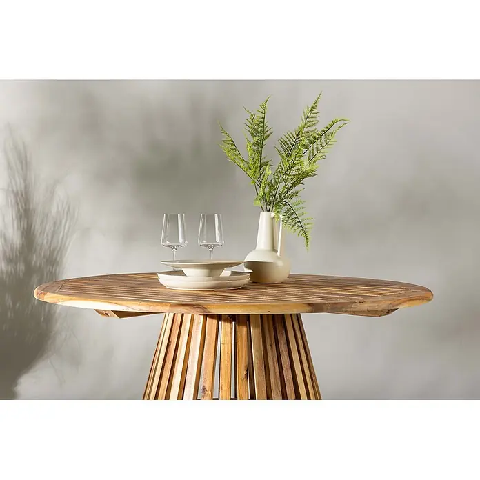 Ebuy24 Gartentisch rund Lumpur - Ø x H: 120 x 75 cm, Akazie, Natur, Stapelbar - Runder Holztisch mit Lamellenfuß, gedeckt mit Geschirr, Gläsern und Farnvase.