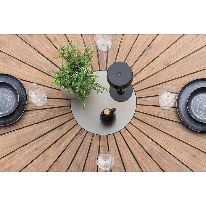 Ebuy24 Gartentisch rund Rosario - Ø x H: 140 x 75 cm, Akazie, Braun, Stapelbar - Runder Holzlamellentisch mit zentraler grauer Einlage, mit Geschirr und Pflanze gedeckt.