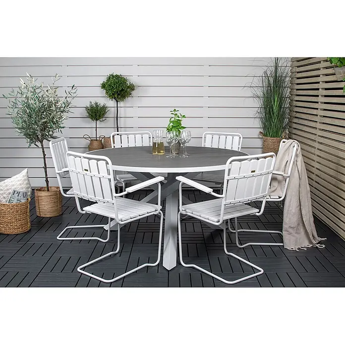 Ebuy24 Gartentisch rund Parma - Ø x H: 140 x 73 cm, Aintwood, Aluminium, Weiß, Stapelbar - Weiße Outdoor-Essgruppe mit rundem dunkelgrauem Tisch und sechs weißen Lattenstühlen auf einer dunklen Terrasse.