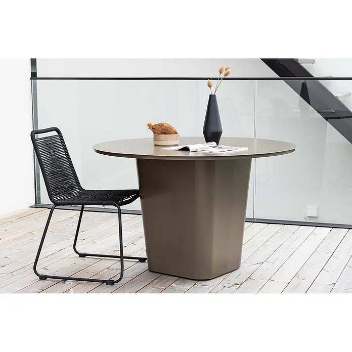 Ebuy24 Gartentisch rund Santa Fe - Ø x H: 120 x 75 cm, Aluminium, Braun, Stapelbar - Ein runder olivfarbener Esstisch mit robustem Sockel, kombiniert mit einem schwarzen Seilstuhl auf einer Holzterrasse.