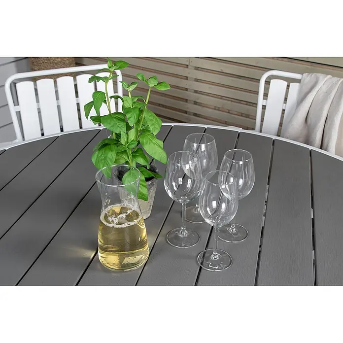 Ebuy24 Gartentisch rund Parma - Ø x H: 140 x 73 cm, Aintwood, Aluminium, Weiß, Stapelbar - Grauer Lamellen-Gartentisch gedeckt mit Weinkanne, Gläsern und Basilikumpflanze.