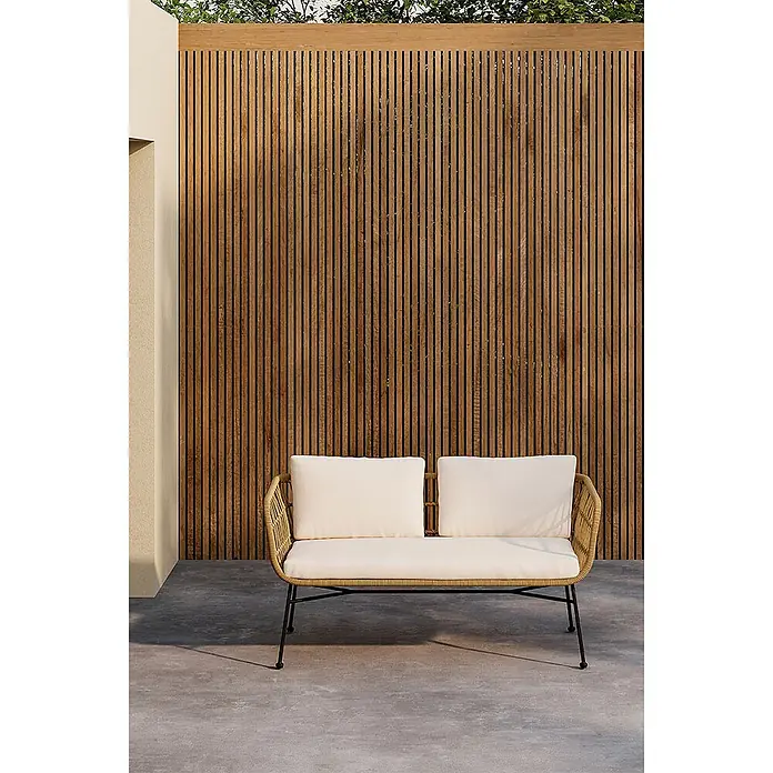 Ebuy24 Loungesofa Isola - B x T x H: 67 x 142 x 71 cm, Polyester.Rattan.Stahl., Natur - Outdoor-Sofa in Rattan-Optik mit schwarzem Gestell und cremefarbenen Polstern auf einer Terrasse vor einer Holzlattenwand.