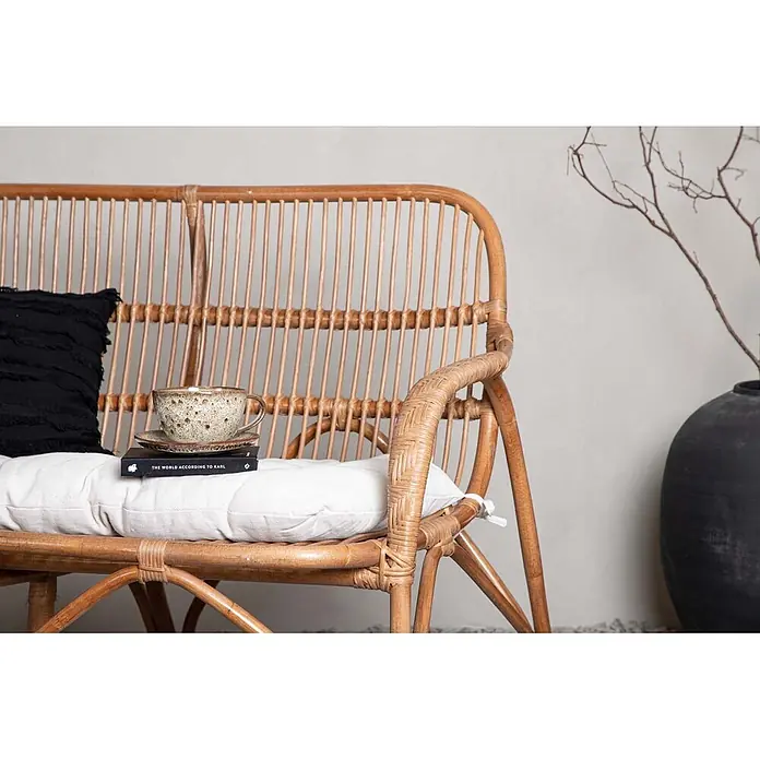 Ebuy24 Loungesofa Nella - B x T x H: 82 x 130 x 93 cm, Rattan., Natur - Natürliche Rattanbank mit weißem Kissen und schwarzem Polster, darauf ein Buch und eine Keramiktasse, bildet einen gemütlichen Sitzbereich.