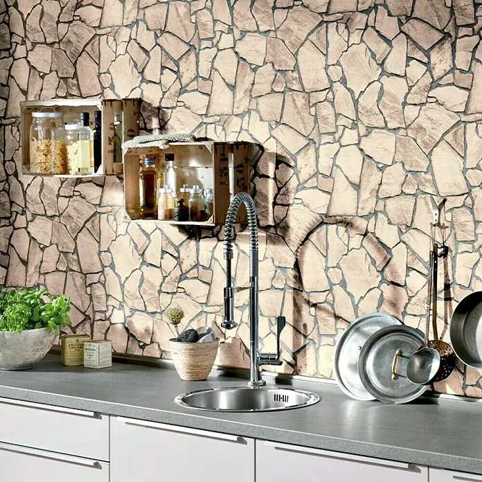 A.S. Création Vliestapete Wood-n-Stone - Beigebraun/Grau, Steinoptik, 10,05 x 0,53 m - Küchenansicht mit Spüle, Armatur und Utensilien vor einer Steinwand. Regale mit Küchenvorräten an der Wand.