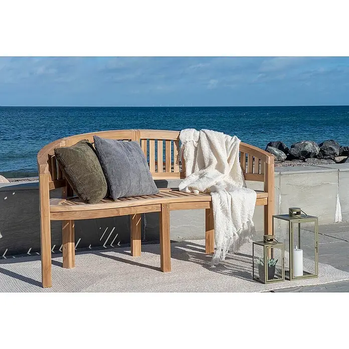 Ebuy24 Gartenbank Boca - B x T x H: 60 x 150 x 85 cm, Teakholz., Teak Dekor - Gebogene helle Holzgartenbank mit olivfarbenen und grauen Kissen, einer weißen Decke und dekorativen Laternen, auf einem Teppich am Meer platziert.