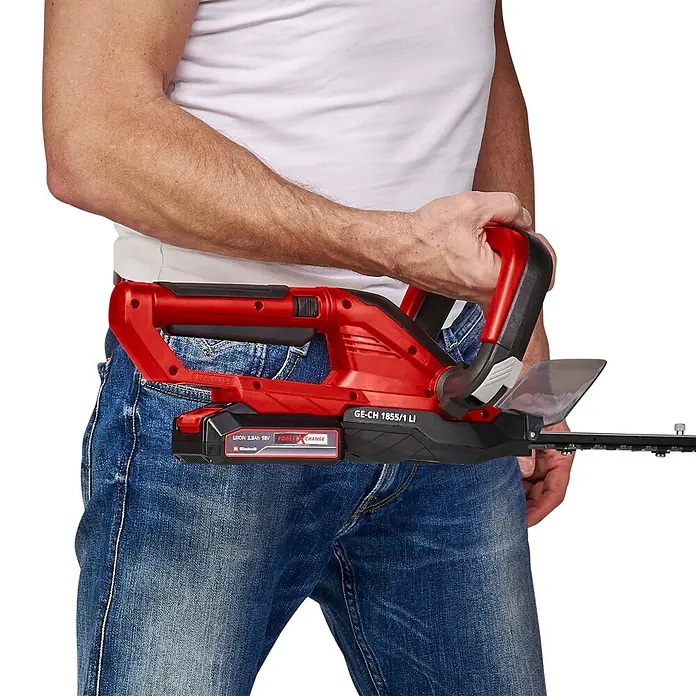 Einhell Power X-Change 18V Akku-Heckenschere GC-CH 1855/1 LI - 18 V, Li-Ionen, 1 Akku, Schnittlänge: 55 cm - Rote und schwarze Akku-Heckenschere, von einer Person in Jeans gehalten, zeigt kompaktes Design und Akku.