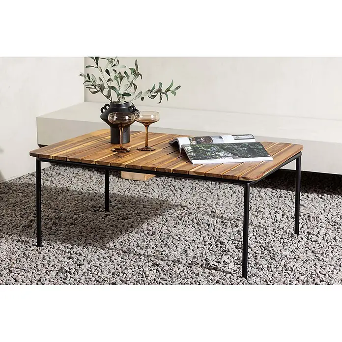 Ebuy24 Garten-Loungetisch Penh - Akazie, Natur, Stapelbar, L x B x H: 100 x 65 x 40 cm - Kaffeetisch mit Holzlamellenplatte und schwarzen Metallbeinen, auf Kies, dekoriert mit Vase, Gläsern und Magazin.