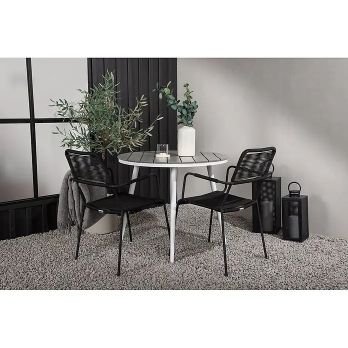 Ebuy24 Gartentisch rund Break - Ø x H: 90 x 74 cm, Aluminium, Weiß, Stapelbar - Ein Outdoor-Bistro-Set mit rundem Tisch aus grauen Latten und weißen Beinen sowie zwei schwarzen geflochtenen Stühlen mit schwarzen Beinen auf einer Kiesterrasse.