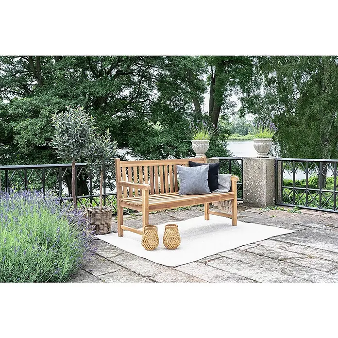 Ebuy24 Gartenbank Cabo - B x T x H: 150 x 150 x 92 cm, Teak., Holz - Hölzerne Gartenbank mit grauen und schwarzen Kissen auf einem Terrassenteppich, umgeben von Pflanzen.