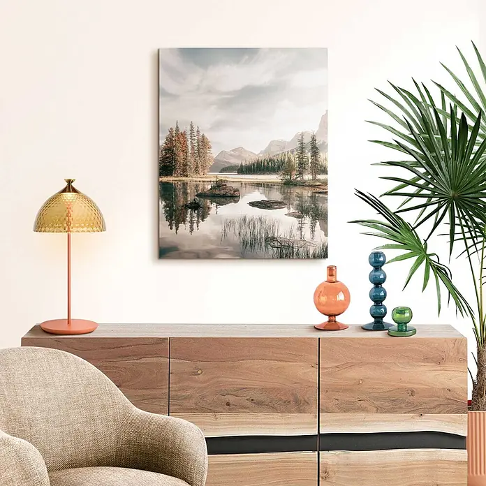 Reinders Decopanel - Spirit Island, B x H: 60 x 90 cm - Gold-orange Tischlampe mit gehämmertem Schirm auf einem Holzschrank neben einem Landschaftsbild.