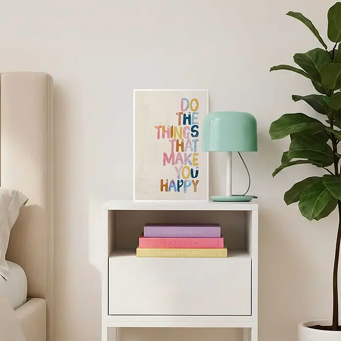 Reinders Bild Slim Frame White - Happy Things, B x H: 20 x 30 cm - Ein gerahmter Druck mit dem motivierenden Zitat „DO THE THINGS THAT MAKE YOU HAPPY“ in farbenfrohen Buchstaben, auf einem Nachttisch mit Lampe und Büchern.