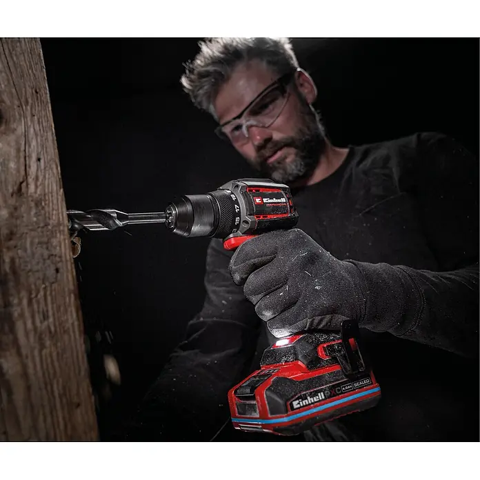 Einhell Professional Power X-Change 18V Akku-Schlagbohrschrauber TP-CD 18/50-C Li-i BL - Solo - 18 V, Ohne Akku, 50 Nm - Rote und schwarze Einhell Akku-Bohrmaschine, von einer behandschuhten Hand gehalten, bohrt in einen Holzbalken, Licht an.