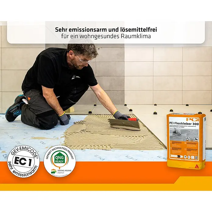 PCI Flexkleber 300 20 kg C2E S1 Großformat - 20 kg - Ein Arbeiter trägt PCI Flexkleber 300 Fliesenkleber für großformatige Fliesen auf einen Boden auf, mit dem orange-gelben Produktsack daneben.