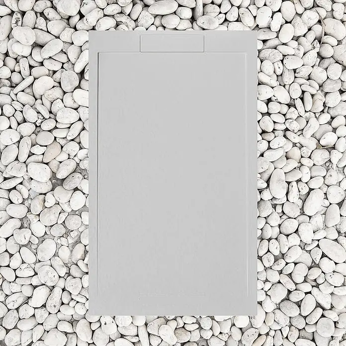 FRASCIO New Tecnology Duschwanne Duschwanne - L x B: 1.400 x 900 mm, Verbundwerkstoff, Grau - Hellgraue rechteckige Harz-Duschwanne, umgeben von weißen Kieselsteinen.