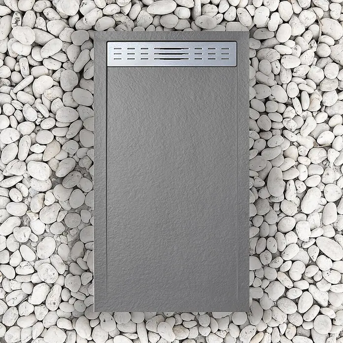 FRASCIO New Tecnology Duschwanne Duschwanne - L x B: 1.200 x 900 mm, Verbundwerkstoff, Grau - Graue strukturierte Duschwanne mit rechteckigem Metallablaufrost, umgeben von weißen Kieselsteinen.