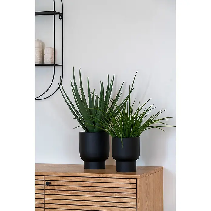 Tinkaro Übertopf rund - Außenmaß (Ø x H): 16 x 19 cm, schwarz, Metall - Zwei Kunstpflanzen (Aloe Vera, Gras) in schwarzen Töpfen auf einem hellen Holzschrank.