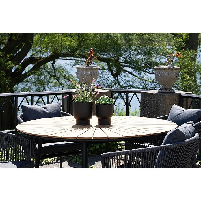 Tinkaro Übertopf rund - Außenmaß (Ø x H): 16 x 19 cm, schwarz, Metall - Gartensitzgruppe mit ovalem Holztisch und dunkelgrauen Seilstühlen mit Kissen, auf einer Terrasse mit Seeblick.