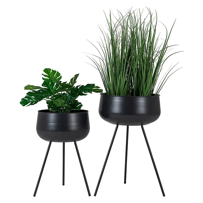 Tinkaro Übertopf rund Blumentopfständer - schwarz, Stahl - Zwei schwarze Metall-Pflanzgefäße auf Ständern, eines mit künstlicher Monstera-Pflanze und das andere mit hohem, grasartigem Kunstlaub.