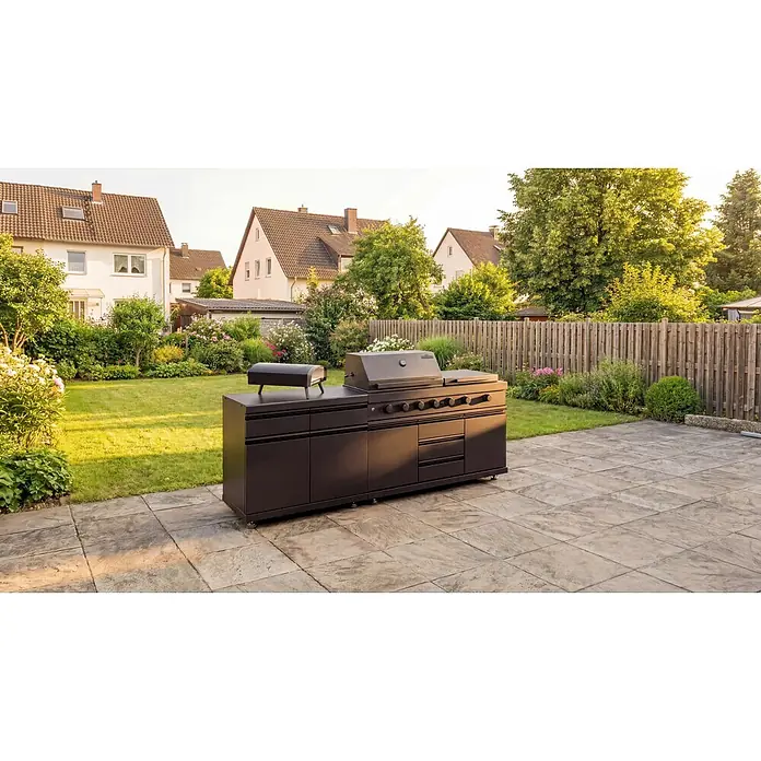 Kingstone Cube Outdoorküche II - 3 -tlg., Stahl, Sintered Stone, Schwarz, Material Grillfläche: Gusseisen, Anzahl Brenner: 7 Stk. - Schwarze Outdoor-Küche mit Grill und Pizzaofen auf einer Terrasse in einem grünen Garten.