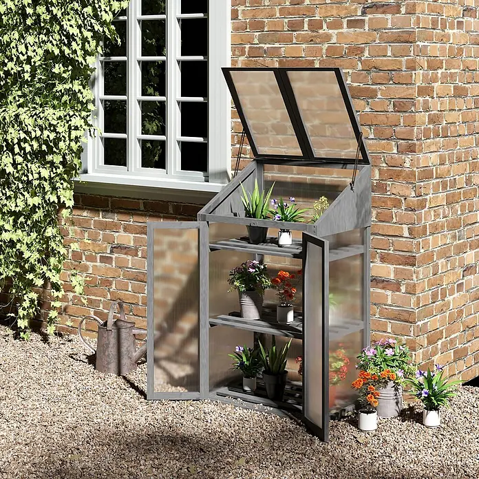 Outsunny Gewächshaus - 70 x 50 cm, Material Seitenwand: Kunststoff, 4 mm, Grau - Graues Holz-Minigewächshaus mit lichtdurchlässigen Paneelen und aufklappbarem Dach, gefüllt mit Topfpflanzen, im Freien auf Kies.