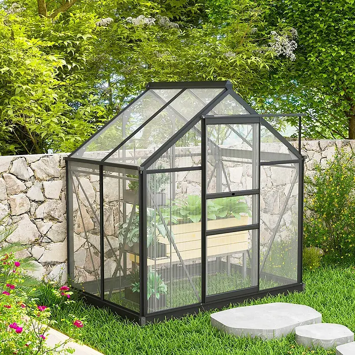 Outsunny Gewächshaus - Außenmaß inkl. Dachüberstand (B x T): 190 x 132 cm, Material Seitenwand: Kunststoff, 4 mm, Grau - Ein kompaktes Gewächshaus mit schwarzem Rahmen und klaren Paneelen, gefüllt mit Pflanzen, steht in einem üppigen Garten an einer Steinmauer.