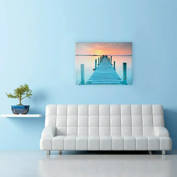 ProArt Sea & Mood Decopanel - Steg, B x H: 115 x 75 cm - Das blaue Wohnzimmer mit weißem Sofa, einem Bonsai und einem Wandbild mit Steg lädt zum Entspannen ein. Die Dekoration verleiht dem Raum eine beruhigende Atmosphäre.
