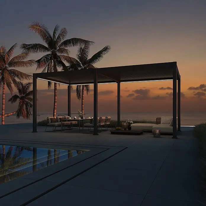 Weide Pergola Deluxe freistehend 3,6 x 5,3 m Anthrazit Aluminium - B x T: 530 x 360 cm, Farbe Gestell: Sandpapier FinishAnthrazit / RAL Farbcode 7024, Aluminium - Moderne dunkle Metallpergola mit integrierter LED-Beleuchtung über Ess- und Loungebereich am Meer bei Dämmerung.