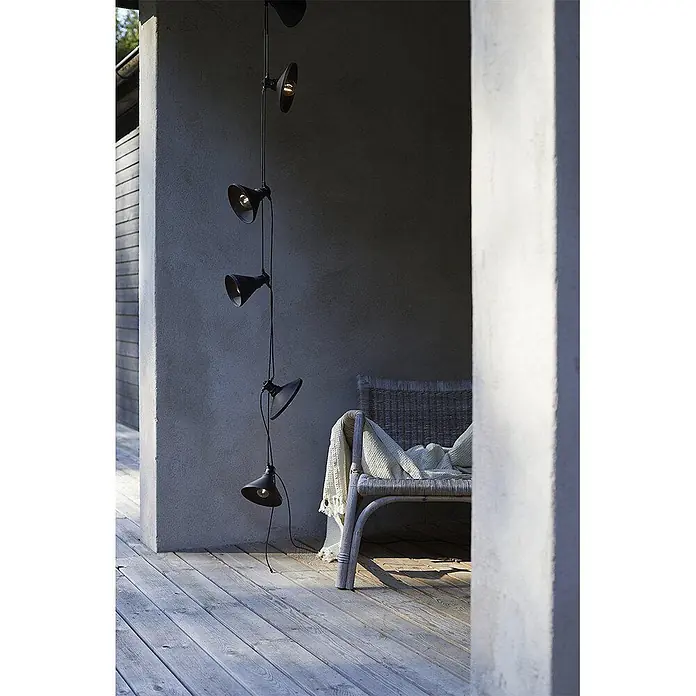 PR Home LED-Lichterkette Daphne -  - Schwarze Outdoor-Lichterkette mit fünf Spot-Schirmen hängt vertikal an einer Wand neben einem Korbstuhl auf einem Holzdeck.