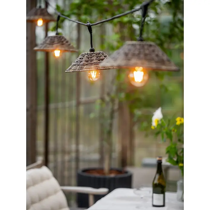 PR Home LED-Lichterkette Flex out -  - Outdoor-Lichterkette mit geflochtenen Korbschirmen, die eine Terrasse mit Tisch und Stuhl beleuchtet.