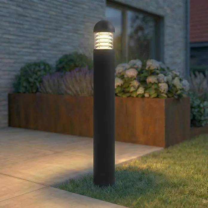 Lucande Außenlaterne Skagena - 12 x 12 x 90 cm - Moderne schwarze Pollerleuchte mit geripptem Kopf, die einen Gartenweg und Rasen im Außenbereich beleuchtet.