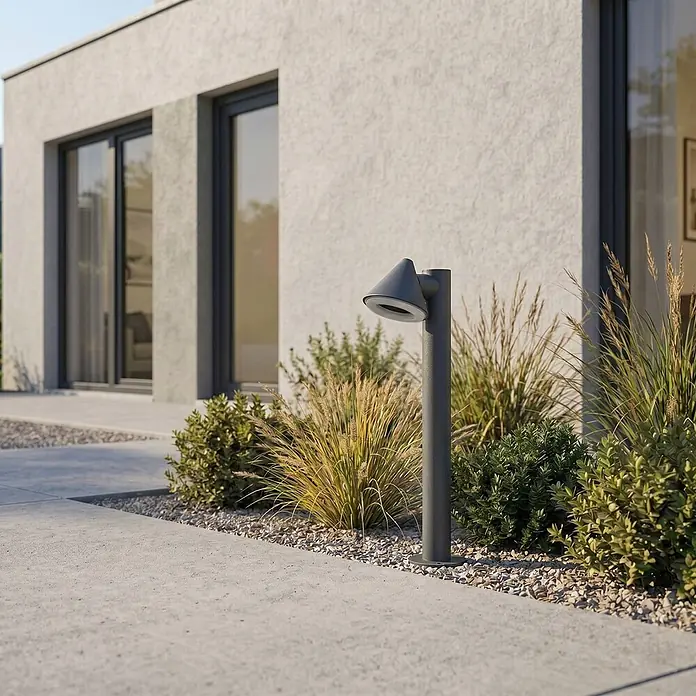 Lindby Außenlaterne Soran -  - Dunkelgraue konische Gartenwegleuchte beleuchtet einen Außenweg neben moderner Architektur und üppigen Pflanzen.