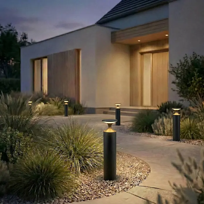 Lucande Außenlaterne Navor -  - Schwarze Wegeleuchten mit goldenen Akzenten beleuchten einen modernen Hauseingang und Gartenweg in der Dämmerung.