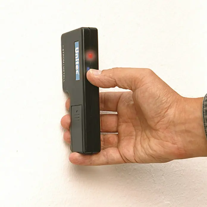 Profi Depot Metall- & Leitungssuchgerät 2 in 1 - Akustisches Signal - Hand hält einen Unitec-Detektor an einer Wand, der auf Strom und Metall reagiert, was durch eine rote LED angezeigt wird.