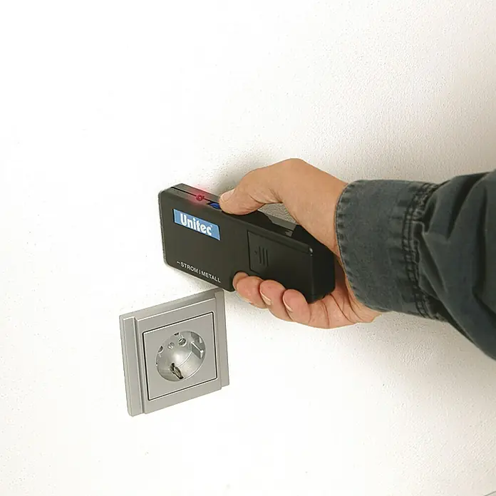 Profi Depot Metall- & Leitungssuchgerät 2 in 1 - Akustisches Signal - Ein Mann hält ein Unitec Strom- und Metallsuchgerät vor einer Steckdose. Das Gerät leuchtet rot, was auf Strom hindeutet.