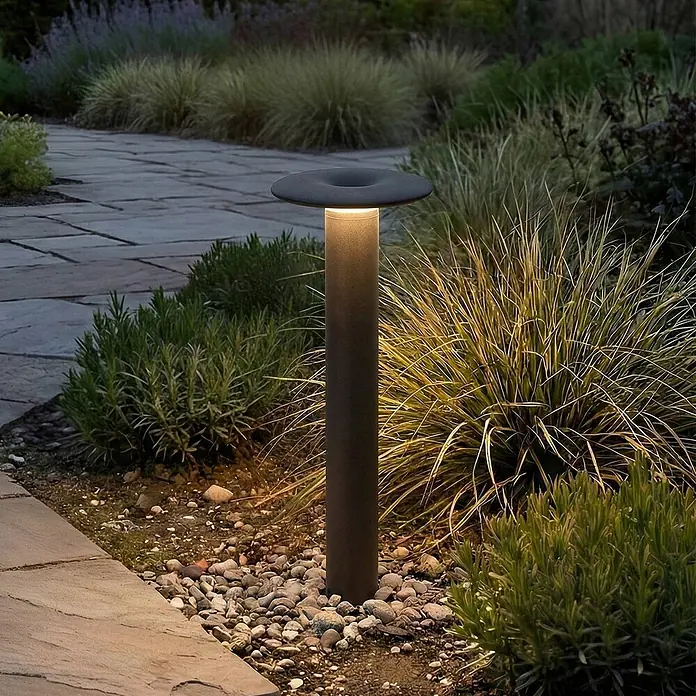 Lucande Außenlaterne Haloa -  - Dunkle Metall-Pollerleuchte, die nachts einen Gartenweg und Pflanzen beleuchtet.