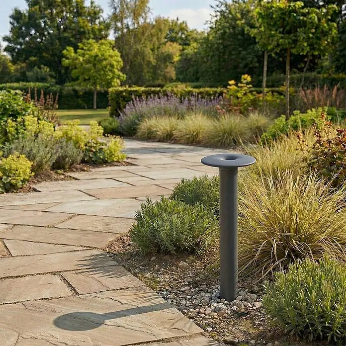 Lucande Außenlaterne Haloa -  - Dunkelgraue Wegeleuchte mit minimalistischem Design, entlang eines Steinweges im Garten zwischen Pflanzen und Gräsern platziert.