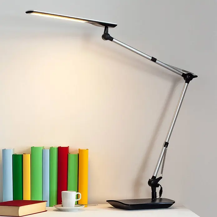 Lindby Tischleuchte Felipe - L x B x H: 36 x 16 x 49 cm, alu / grau / zink - Eine moderne silberne und schwarze LED-Schreibtischlampe beleuchtet einen Schreibtisch mit bunten Büchern und einer Tasse, ideal zum Lesen oder Arbeiten.