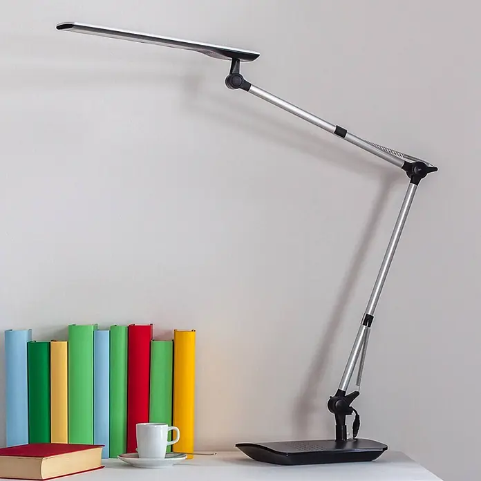 Lindby Tischleuchte Felipe - L x B x H: 36 x 16 x 49 cm, alu / grau / zink - Moderne Schreibtischlampe in Silber und Schwarz auf weißem Tisch, beleuchtet bunte Bücher und eine Tasse.