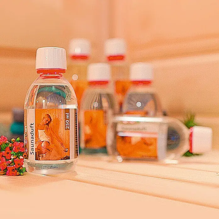 Karibu Saunaduft - Duft: Lemongras, 250 ml - Eine Flasche Saunaduft mit floralen Akzenten, umgeben von weiteren Flaschen, die ein entspannendes Saunaerlebnis versprechen.