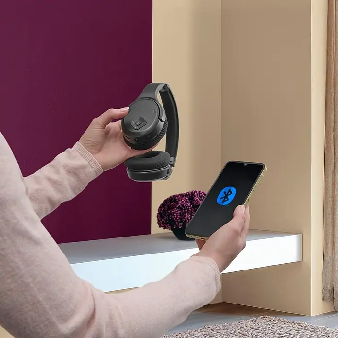 Hama Kopfhörer Over Ear Kabellos Funk Bluetooth Lautstärkeregelung TV - Schwarz - Person koppelt schwarze Over-Ear-Kopfhörer mit einem Smartphone, das das Bluetooth-Symbol anzeigt.