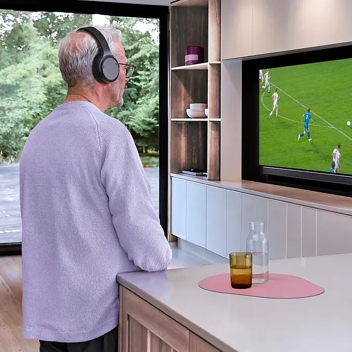 Hama Kopfhörer Over Ear Kabellos Funk Bluetooth Lautstärkeregelung TV - Schwarz - Ein Mann trägt dunkelgraue Over-Ear-Kopfhörer, während er fernsieht und personalisierten Sound genießt.