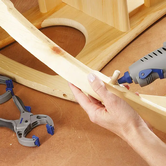 Dremel Heißklebepistole 940-3 - Durchmesser Klebepatrone: 11 mm - 12 mm, Aufheizzeit: 5 min - 7 min, Arbeitstemperatur: 195 °C - Bild zeigt die Verwendung einer Heißklebepistole zum Anbringen eines Dübels an einem Holzstück, ideal für Holzbearbeitungsprojekte.