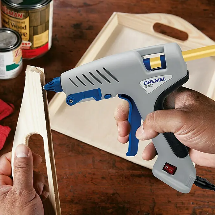 Dremel Heißklebepistole 940-3 - Durchmesser Klebepatrone: 11 mm - 12 mm, Aufheizzeit: 5 min - 7 min, Arbeitstemperatur: 195 °C - Nahaufnahme einer Dremel 940 Heißklebepistole beim Auftragen von Klebstoff auf ein Holzstück, ideal für Heimwerkerarbeiten und Bastelprojekte.
