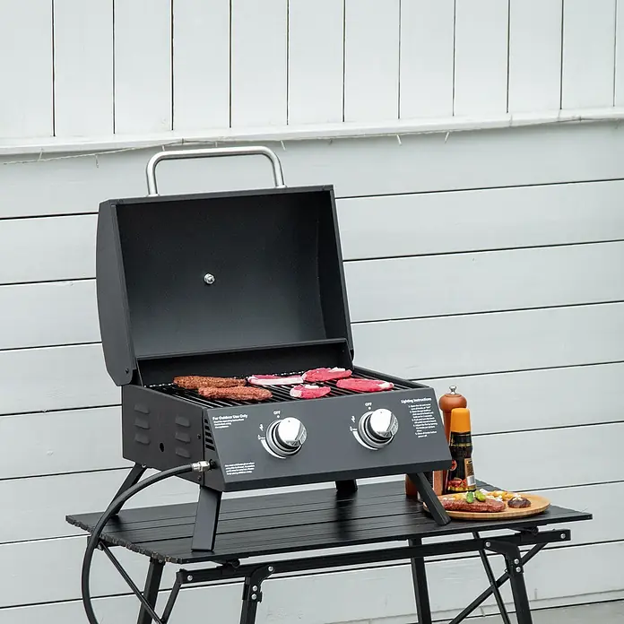 Outsunny Gasgrill - Anzahl Brenner: 2 Stk. - Schwarzer tragbarer Gasgrill auf einem Klapptisch, mit rohem Fleisch auf den Rosten.