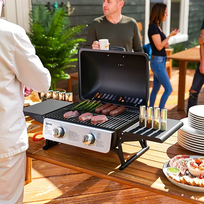 Outsunny Gasgrill - Anzahl Brenner: 2 Stk. - Ein tragbarer Gasgrill mit schwarzem Deckel und silbernem Bedienfeld steht auf einem Holztisch und grillt Speisen bei einem Treffen im Freien.